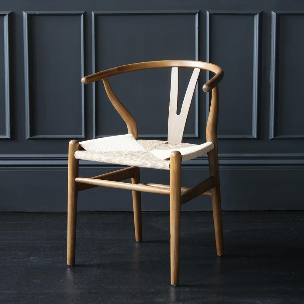 Hans J. Wegner - Chaise Wishbone en bois clair dans une pièce sombre.